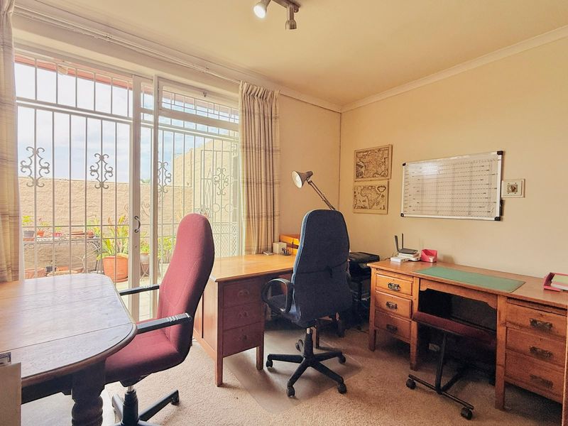 A functional home office space featuring carpet flooring, a ceiling spotlight, and a large sliding glass door with security gate leading to the patio.