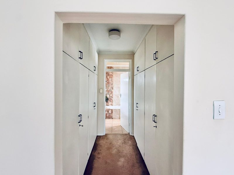 A hallway featuring extensive built-in storage cupboards with a direct view into an adjacent bathroom.