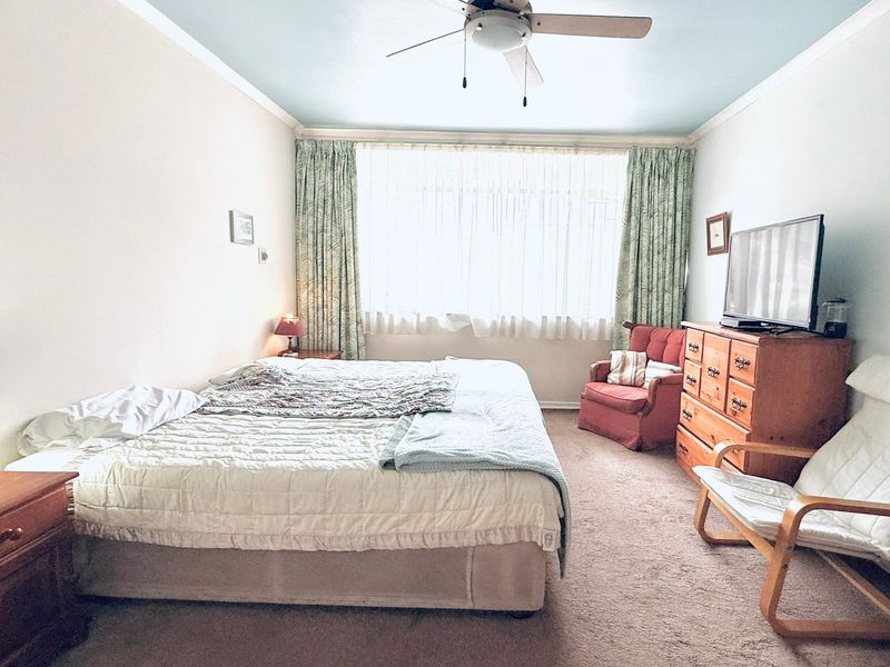 A spacious bedroom featuring carpeted flooring, a ceiling fan, and a large window allowing for natural light.