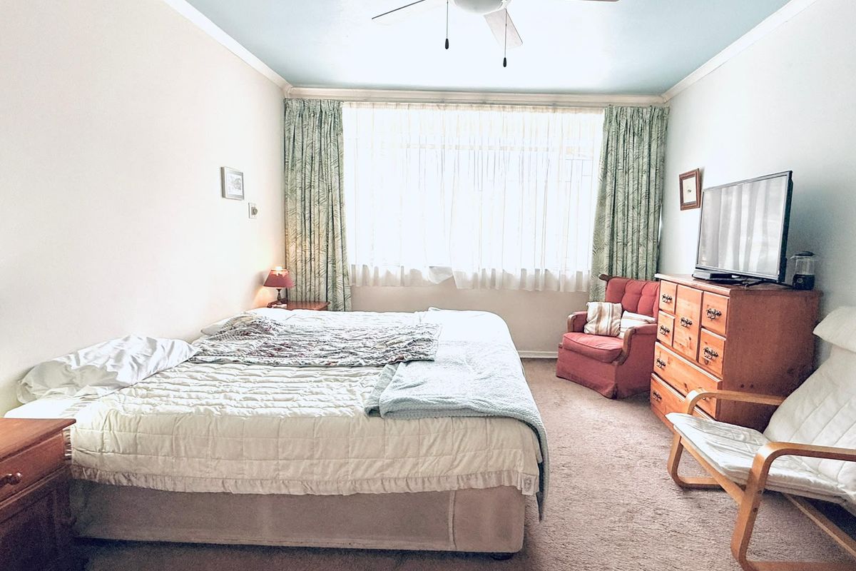 A spacious bedroom featuring carpeted flooring, a ceiling fan, and a large window allowing for natural light.