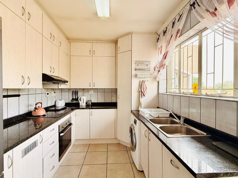 Functional kitchen featuring light wood-finish cabinetry, granite countertops, integrated oven and hob, and a double stainless steel sink with tiled backsplash.