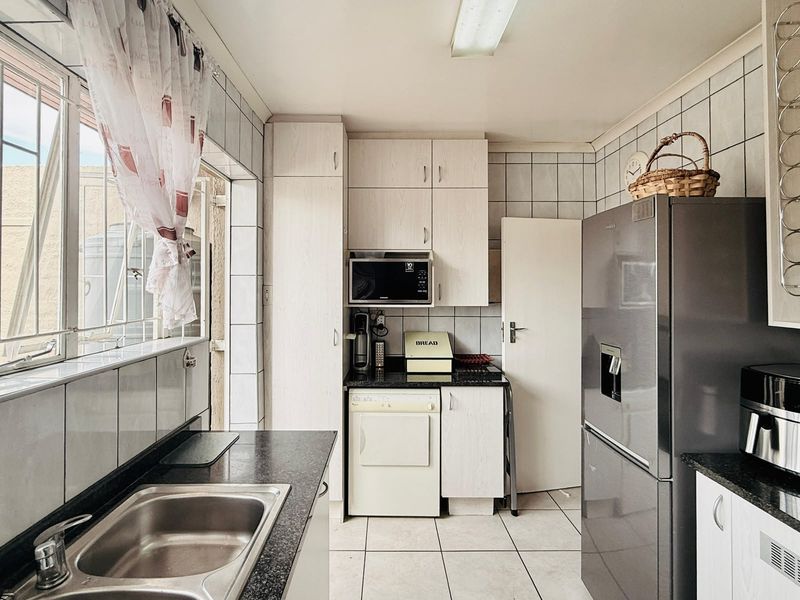 A functional kitchen featuring granite countertops, tiled backsplash, built-in cabinetry, and a stainless steel sink, offering a practical layout for daily meal preparation.