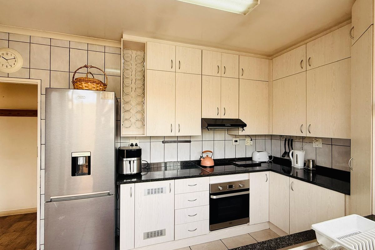 A functional kitchen featuring light wood-finish cabinetry, dark granite countertops, built-in oven, electric hob, and a tiled backsplash.