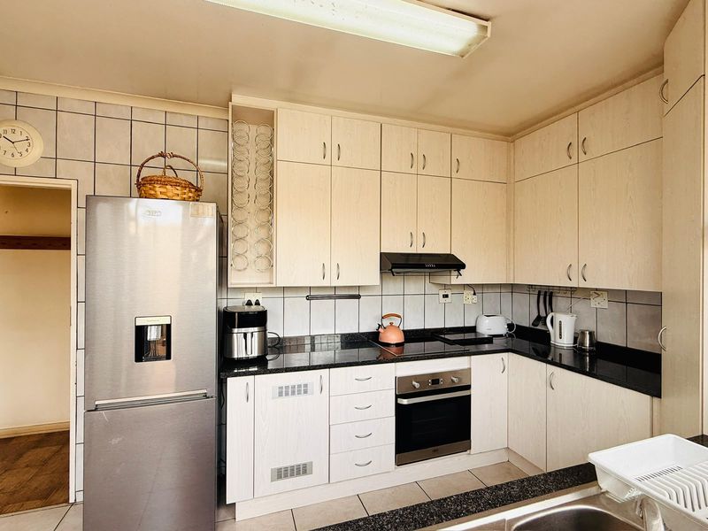 A functional kitchen featuring light wood-finish cabinetry, dark granite countertops, built-in oven, electric hob, and a tiled backsplash.