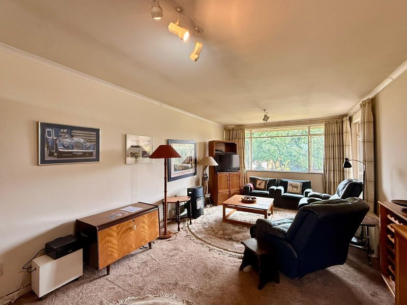 A spacious living room featuring large windows, neutral walls, and carpet flooring, offering a comfortable and well-lit area for relaxation.
