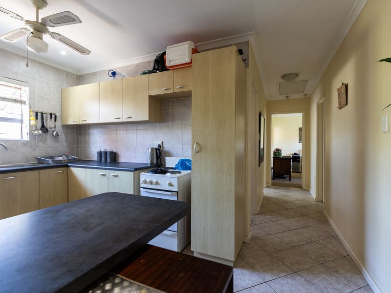 Functional kitchen featuring laminate cabinetry, tiled backsplash, and tiled flooring, with an adjacent hallway leading to other living areas.