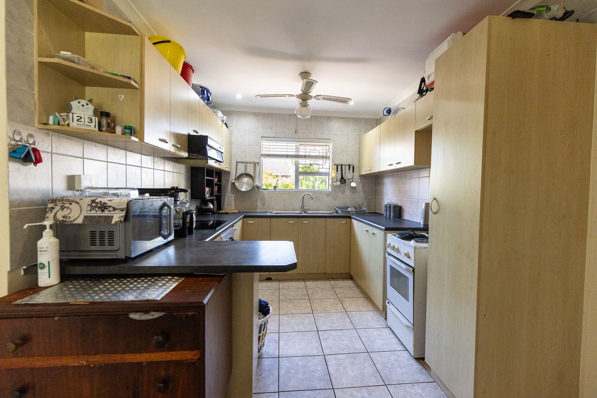 A functional kitchen featuring laminate cabinetry, dark countertops, tiled flooring, and a freestanding oven, offering a practical layout with ample storage space.