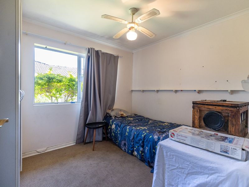 A compact bedroom featuring a ceiling fan, built-in cupboard, and carpeted flooring, offering a functional space with potential for cosmetic updates.