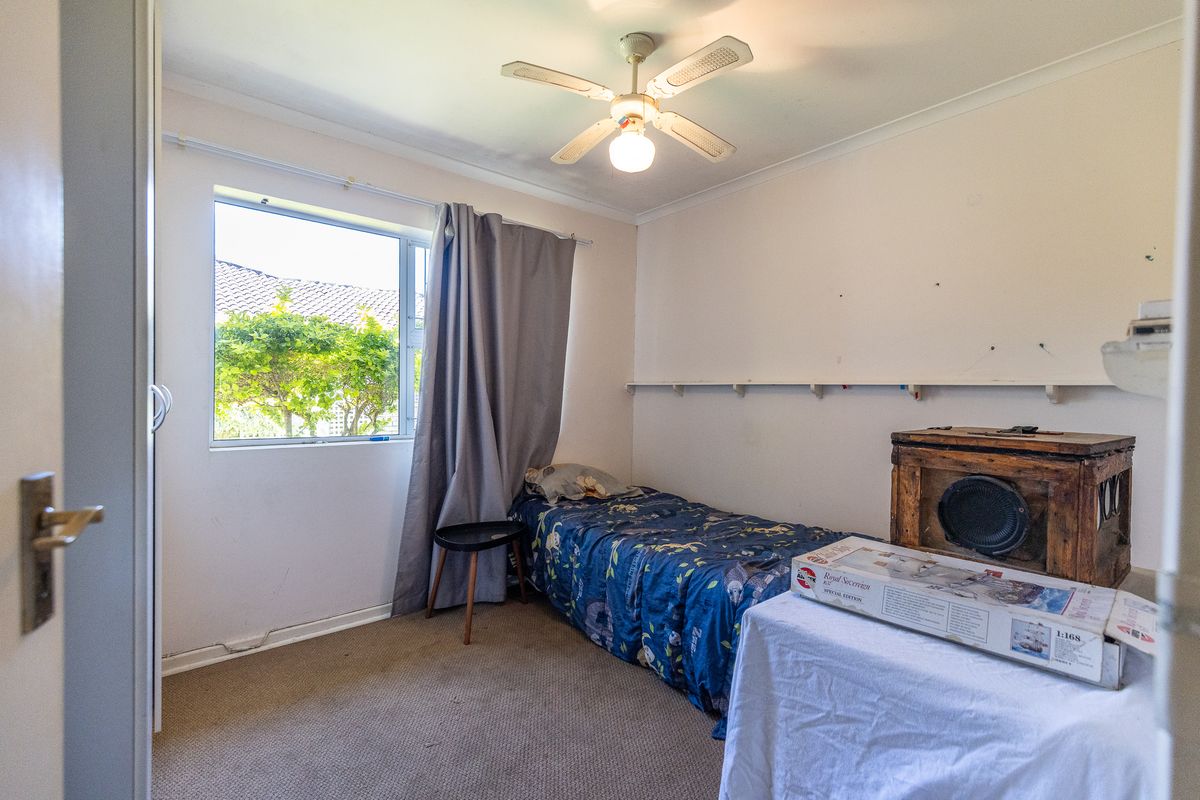 A compact bedroom featuring a ceiling fan, built-in cupboard, and carpeted flooring, offering a functional space with potential for cosmetic updates.