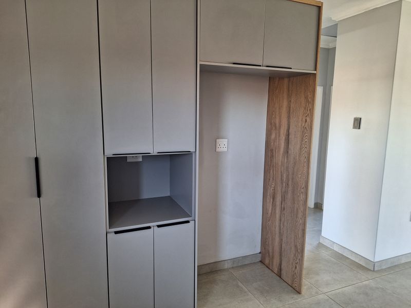 A modern, empty kitchen area featuring sleek built-in cabinetry with a dedicated appliance recess and neutral tiled flooring.