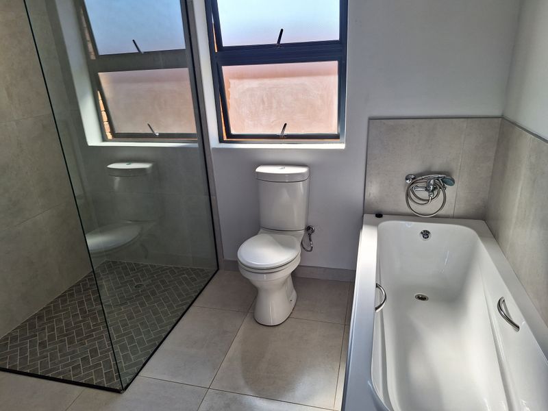 Modern bathroom featuring a glass-enclosed shower, a bathtub with a handheld mixer, and a toilet, finished with neutral floor and wall tiling.