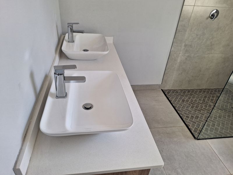 Modern bathroom featuring a double vanity with vessel sinks, chrome fixtures, and a spacious walk-in shower with stylish herringbone tiling.