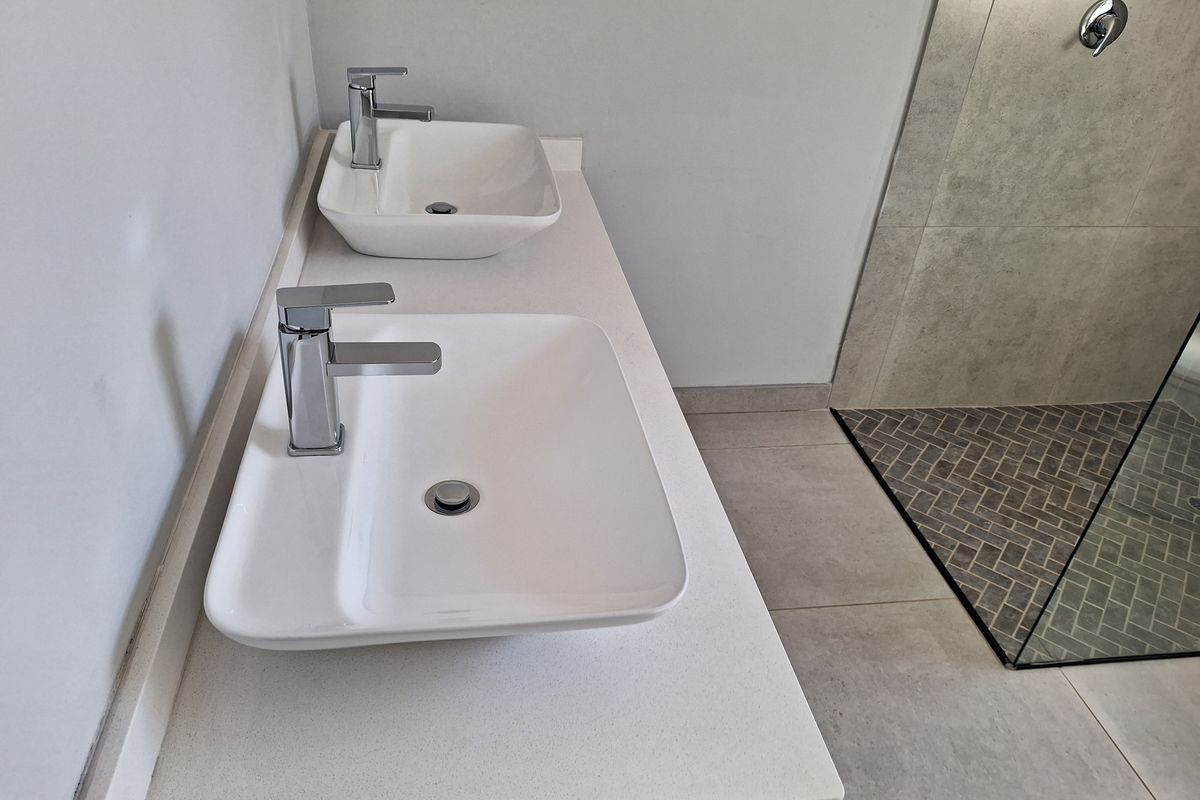 Modern bathroom featuring a double vanity with vessel sinks, chrome fixtures, and a spacious walk-in shower with stylish herringbone tiling.