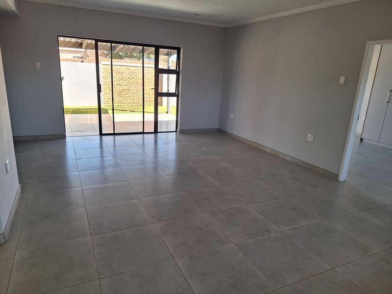 Spacious, empty living area featuring neutral tiled flooring and a large sliding glass door providing access to the outdoor patio.