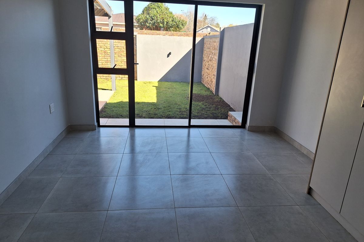 A bright, empty living area featuring large sliding glass doors that open onto a private garden, finished with modern neutral floor tiles.