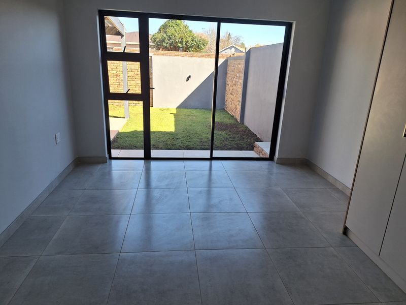 A bright, empty living area featuring large sliding glass doors that open onto a private garden, finished with modern neutral floor tiles.