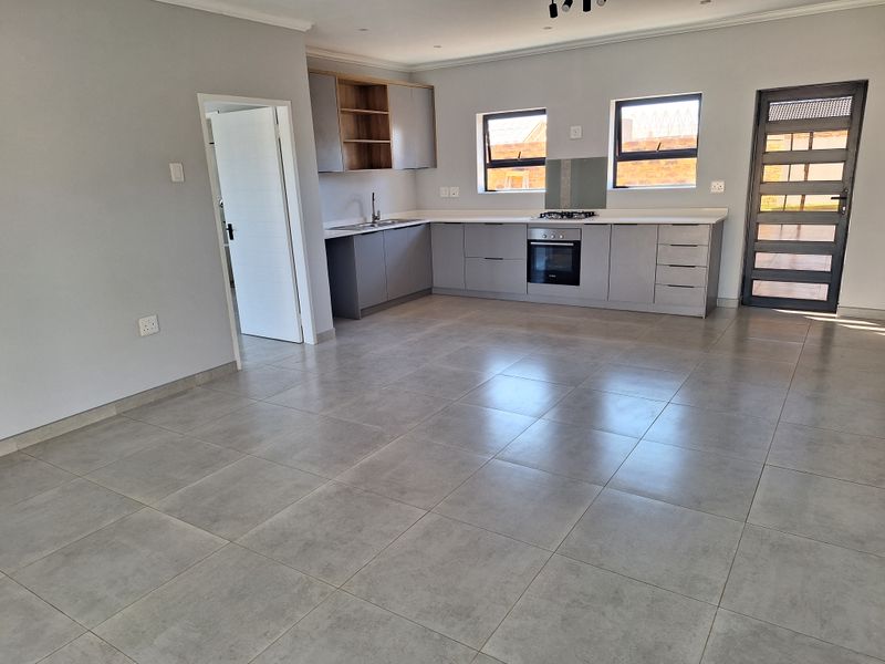 Modern open-plan kitchen featuring sleek grey cabinetry, stone countertops, built-in oven, gas hob, and large format floor tiles in a bright, spacious layout.