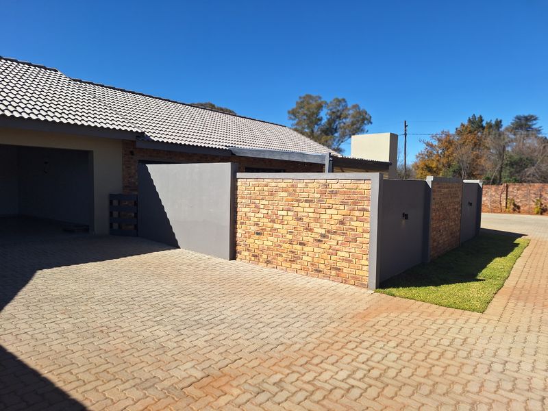 A well-maintained townhouse exterior featuring a paved driveway, modern brick and rendered boundary wall, and a tiled roof.
