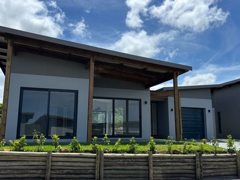 Modern townhouse exterior featuring a skillion roof, timber pergola, sliding glass doors, and a paved driveway with a timber retaining wall.