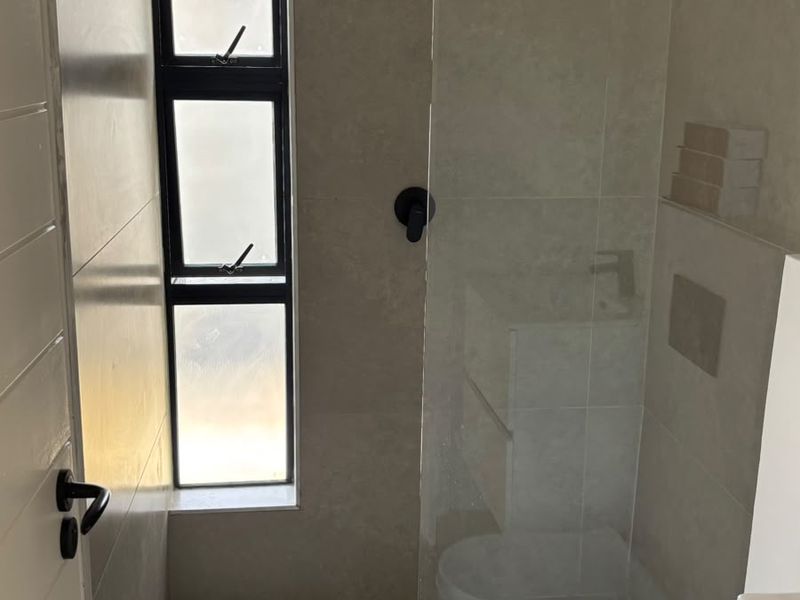 Modern bathroom featuring a walk-in shower with a rain shower head, glass screen, wall-hung toilet, and neutral floor-to-ceiling tiling.