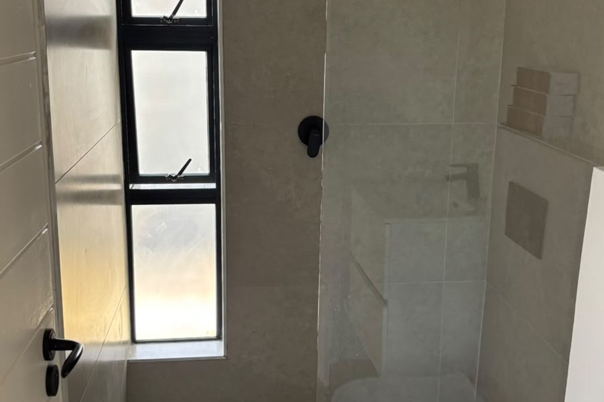Modern bathroom featuring a walk-in shower with a rain shower head, glass screen, wall-hung toilet, and neutral floor-to-ceiling tiling.