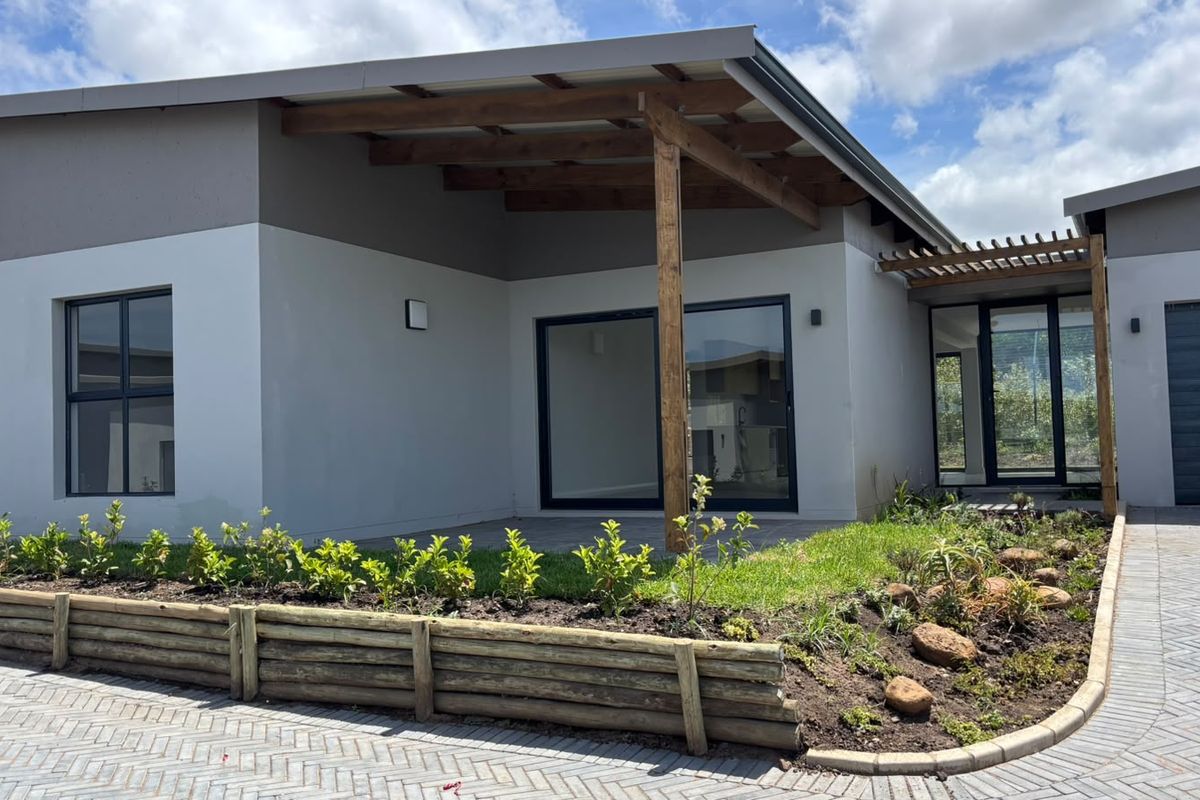 Modern townhouse exterior featuring a timber pergola, paved driveway, and landscaped garden with a retaining wall and sliding glass door entrance.