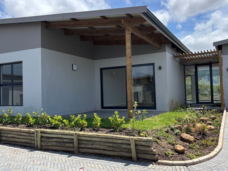 Modern townhouse exterior featuring a timber pergola, paved driveway, and landscaped garden with a retaining wall and sliding glass door entrance.