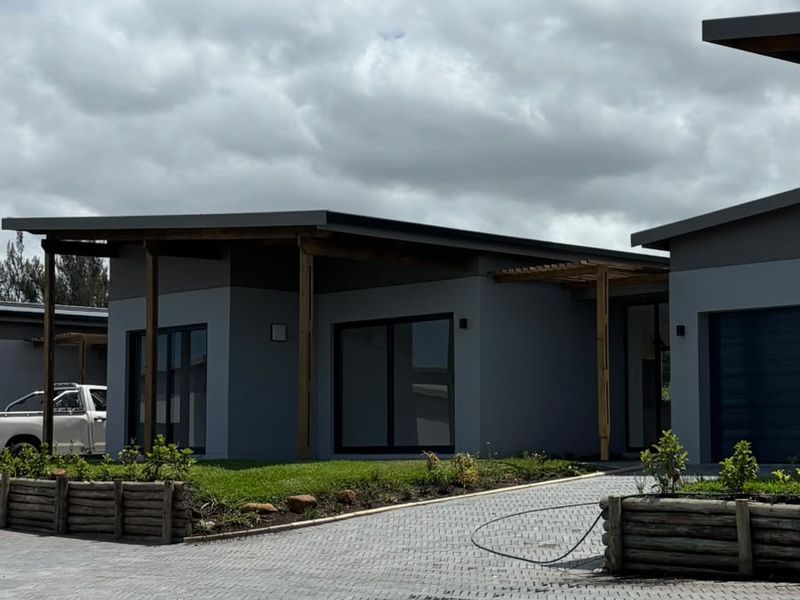 Modern townhouse exterior featuring a paved driveway, timber pergola, and contemporary grey facade with sliding glass doors.