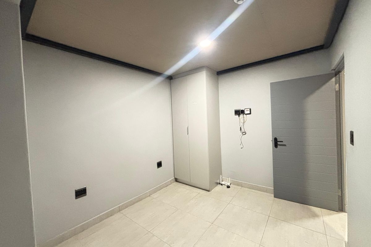 A clean, empty bedroom featuring neutral tiled flooring, a built-in cupboard, and a modern recessed ceiling design.
