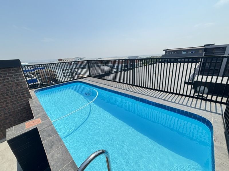 A rooftop swimming pool featuring a tiled surround, metal safety railing, and views of the surrounding urban area.