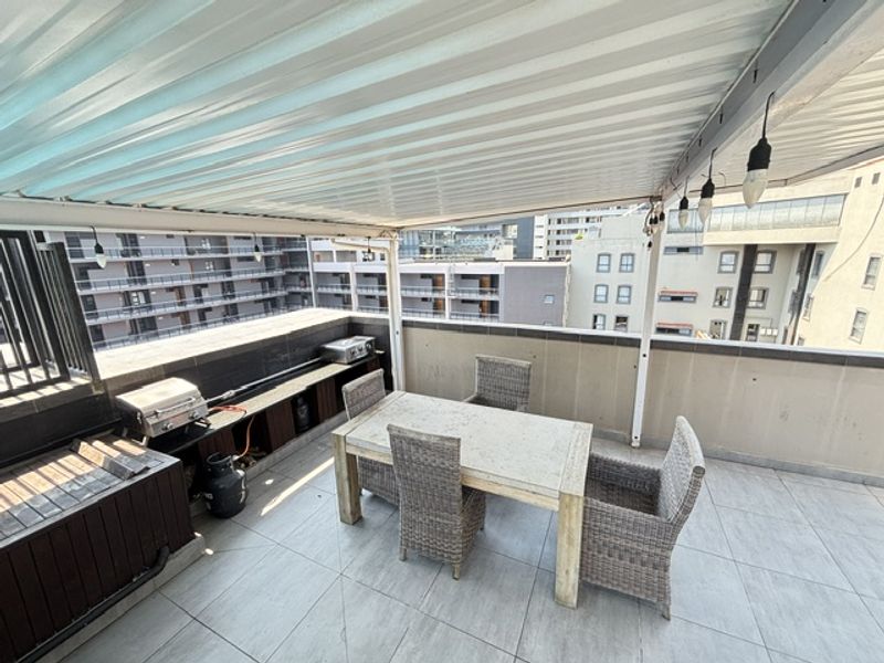 A covered balcony featuring tiled flooring, a built-in counter area, and a protective balustrade, offering an outdoor space for relaxation and dining.