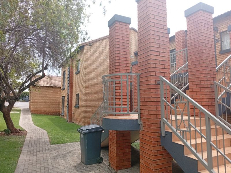 Exterior view of a face brick apartment complex featuring a paved walkway, tiled staircase, and metal balustrades.