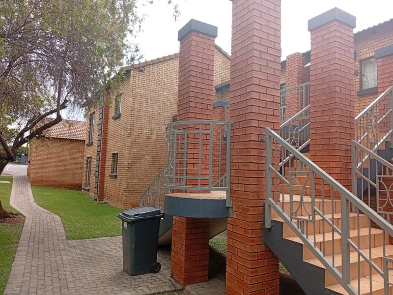 Exterior view of a face brick apartment complex featuring a paved walkway, landscaped lawn, and external staircase with metal balustrades.