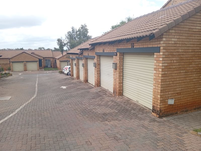 A row of residential garages with brick facades and tiled roofs, situated along a paved driveway in an apartment complex.