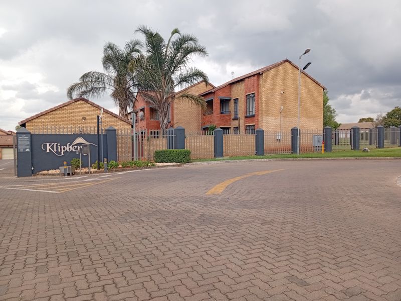 Front exterior view of the Klipberg apartment complex featuring face-brick architecture, secure perimeter fencing, and a paved entrance area.