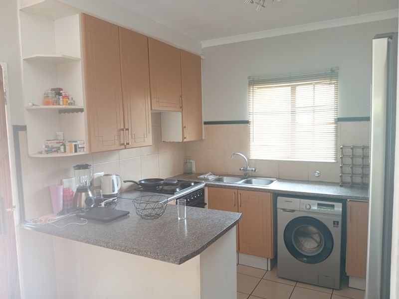 A functional kitchen featuring laminate cabinetry, a double bowl sink, tiled splashbacks, and built-in cooking appliances with space for a washing machine.