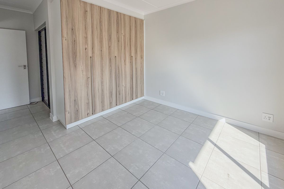 A bright, empty bedroom featuring modern wood-finish built-in cupboards and neutral tiled flooring, offering a clean and versatile space.