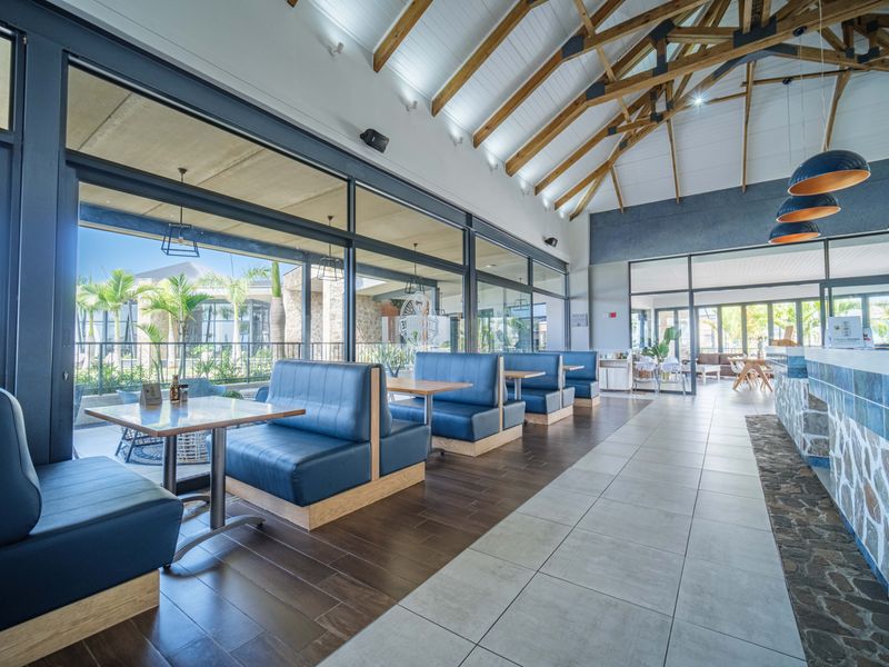 A spacious open-plan area featuring a vaulted timber ceiling with exposed trusses, stone-clad service counter, and large glass doors opening to an outdoor patio.