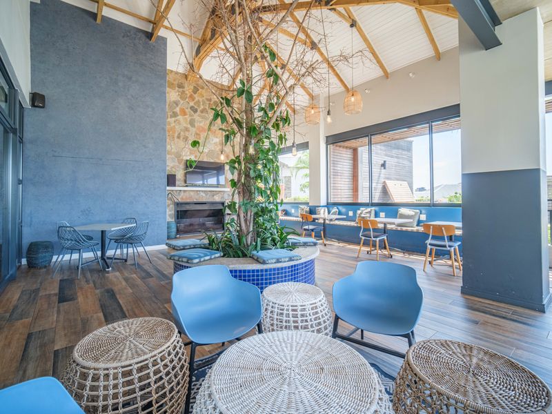 A spacious, modern clubhouse area featuring a vaulted timber ceiling, stone fireplace, and built-in bench seating with large windows providing ample natural light.