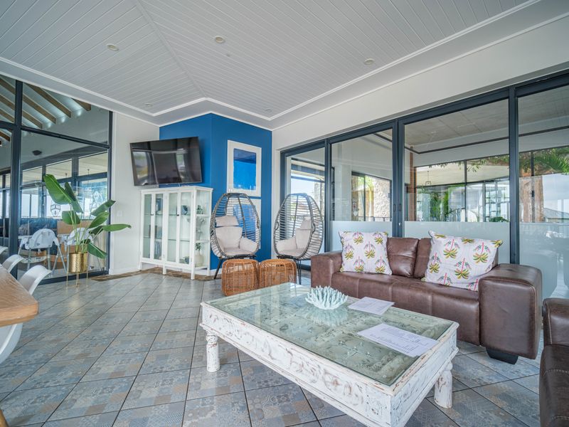 A bright and spacious living area featuring tiled flooring, a tongue and groove ceiling with recessed lighting, and large aluminium framed glass sliding doors.