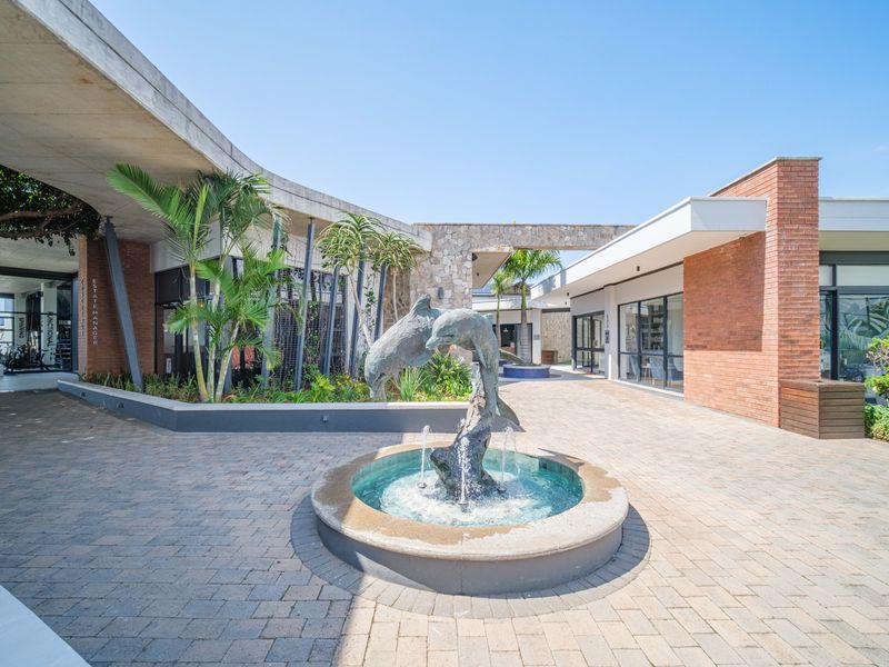 A well-maintained communal courtyard featuring a central dolphin fountain, paved walkways, and modern architectural elements including brick and concrete structures.