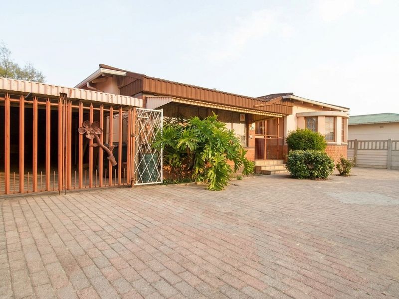 Front exterior view of a single-story house featuring a paved driveway, carport, and secure metal gate entrance.