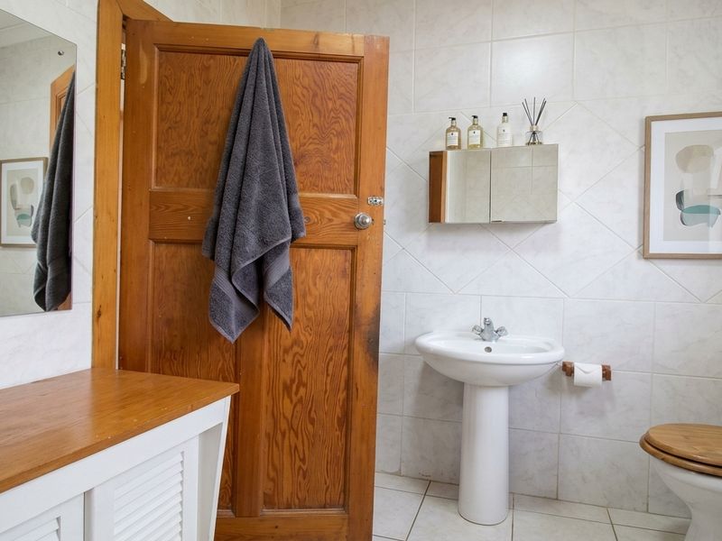 A functional bathroom featuring a pedestal basin, wall-mounted medicine cabinet, tiled walls and flooring, and a wooden vanity cabinet.