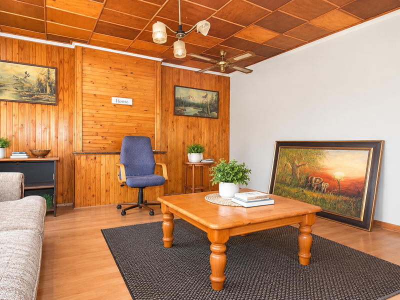 A living room featuring warm timber wall paneling, a matching coffered ceiling, and laminate flooring, creating a traditional and cozy atmosphere.