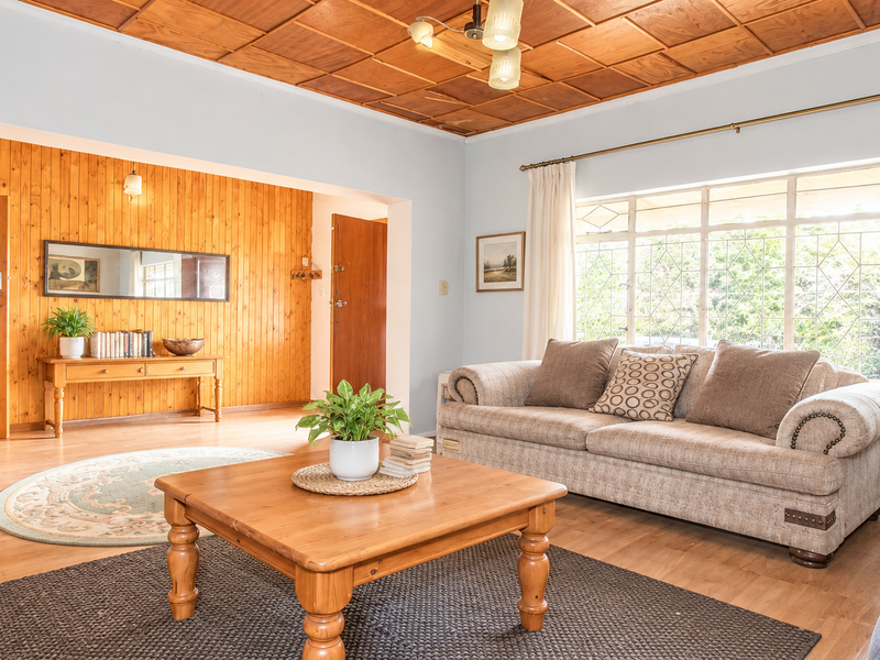 A spacious living room featuring warm wooden wall panelling, a coffered timber ceiling, and large windows that provide ample natural light.