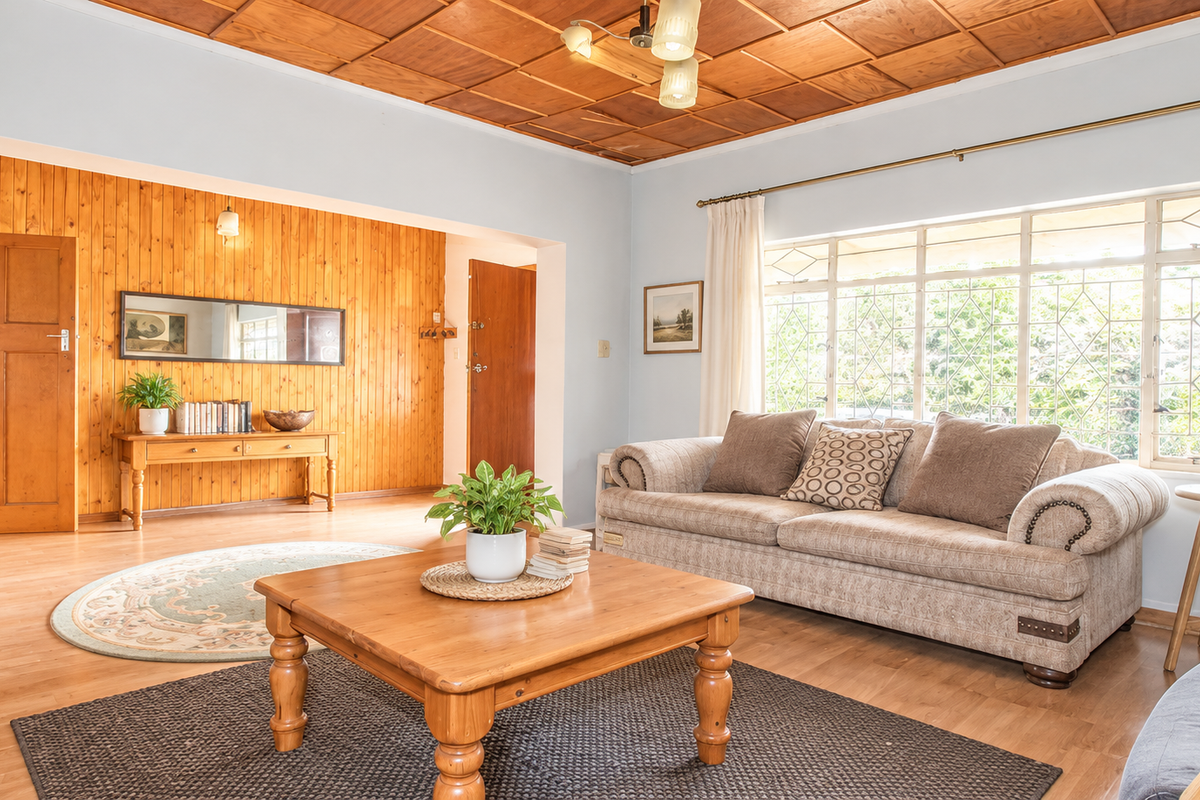 A spacious living room featuring warm wooden wall panelling, a coffered timber ceiling, and large windows that provide ample natural light.