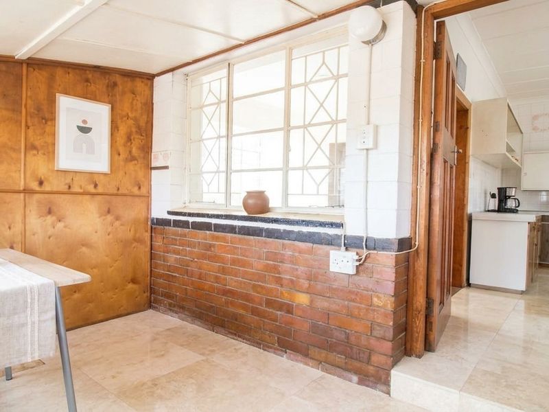 Open plan living and kitchen area featuring exposed brickwork, wood paneling, and tiled flooring, offering a functional layout with direct access between spaces.