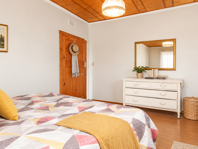 A well-maintained bedroom featuring warm timber ceiling paneling, laminate flooring, and a solid timber door, creating a cozy and inviting atmosphere.