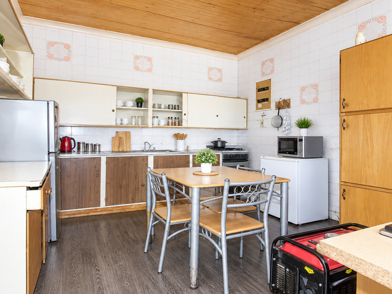 A functional kitchen featuring timber ceiling paneling, tiled splashbacks, built-in cabinetry, and a gas hob, offering a practical layout with potential for modern updates.