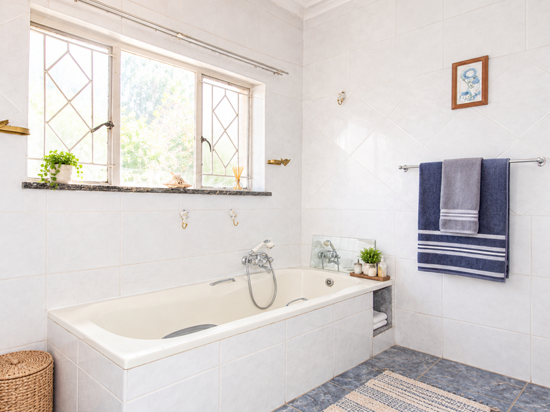 A functional bathroom featuring a built-in bathtub, tiled wall finishes, and a window with security bars.